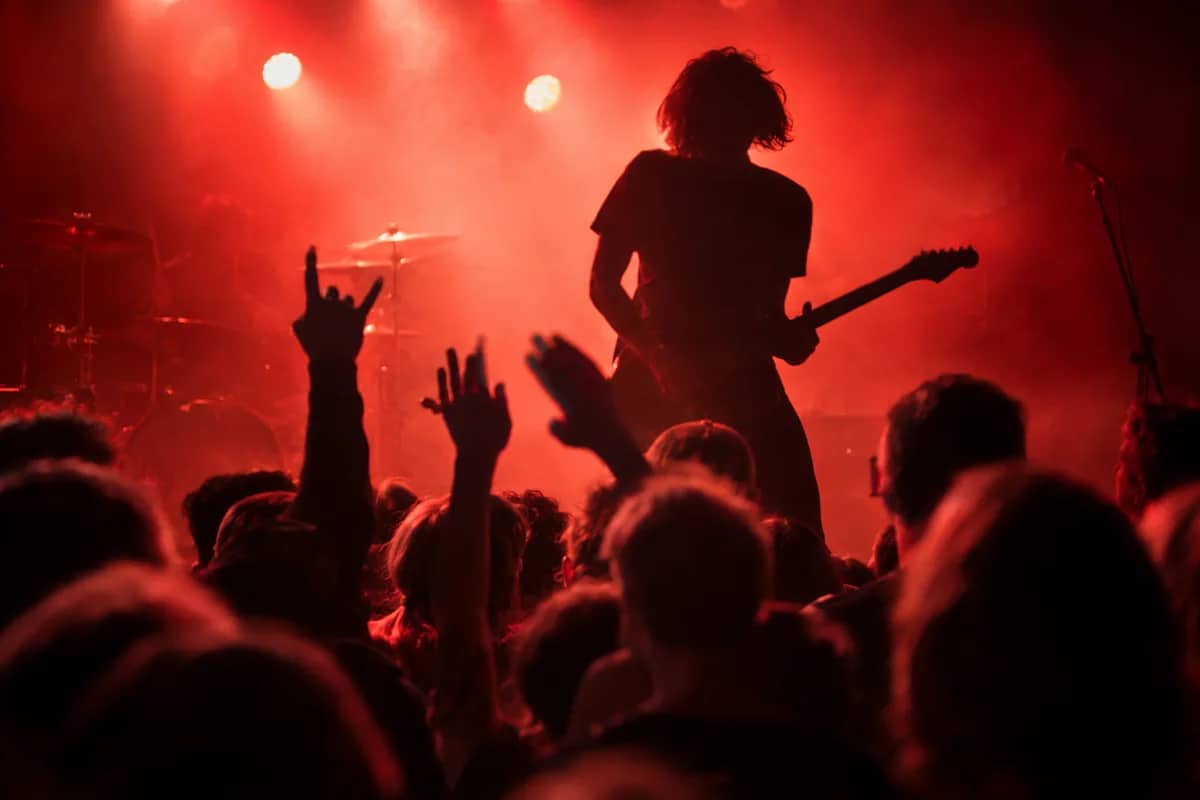 AI-generated illustration Guitarist silhouetted against red stage lights with hands raised in the crowd — AI-generated illustration