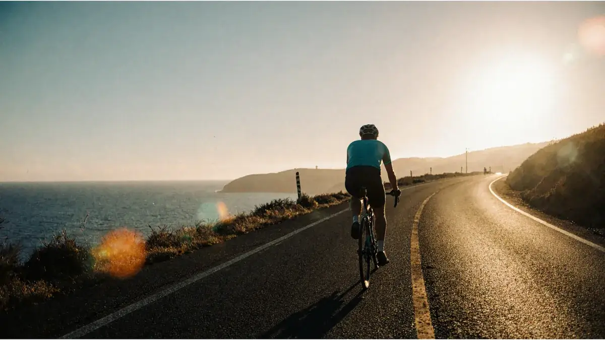 AI-generated illustration Cyclist seen from behind riding a coastal road beside the sea at sunset — AI-generated illustration
